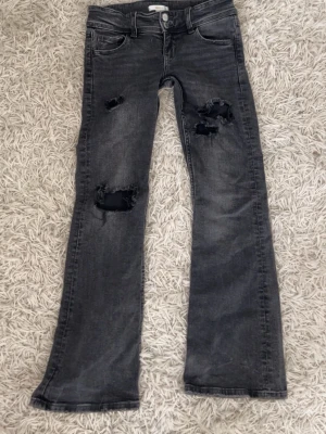Grå slitna jeans från Gina Tricot - Säljer ett par grå jeans från Gina Tricot med slitningar och hål på båda benen. Jeansen har klassisk femficksmodell, raka ben och coolt tvättad look. Perfekta för dig som gillar en avslappnad och trendig stil.