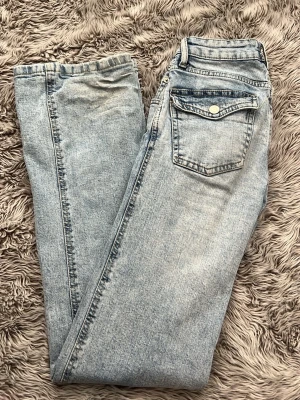 Ljusblå bootcut jeans från 157 - Säljer ett par ljusblå bootcut jeans från 157 med klassisk femficksdesign och en snygg ficka med lock bak. Jeansen har en vintage 90-talskänsla och är tillverkade i denim. Perfekta för dig som gillar retrostil och bekväma jeans.
