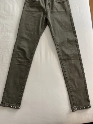 Olivgröna skinny jeans med pärldetaljer - Snygga grå skinny jeans från Zac & Zoe med pärldetaljer längst ner vid bensluten. Jeansen har klassisk femficksmodell och är tillverkade i stretchigt material för en bekväm passform. Perfekta för dig som vill ha något extra till din outfit.