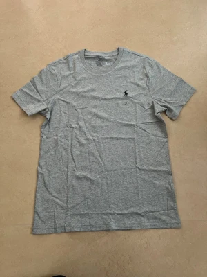 Ralph lauren T-shirt grå storlek medium  - Ny Ralph Lauren t-shirt med klassisk passform. Perfekt basplagg till sommaren.  Oanvänd Väldigt populär modell Enkel att matcha  Skickas snabbt 📦 Rabatt vid köp av flera.