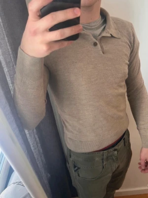 Beige stickad tröja från Morris - Snygg beige stickad tröja från Morris i 100% merinoull. Tröjan har krage och knappar vid halsen samt ribbade muddar vid ärmslut och nederkant. Perfekt för dig som gillar stilrena och klassiska plagg. Storlek M men passar som S