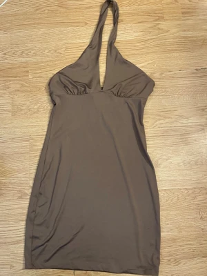 Brun klänning  - En brun kortklänning i ett stretchigt material. Har en v - ringning och ett band som går runt halsen Sparsamt använt, är i mycket fint skick! 💕