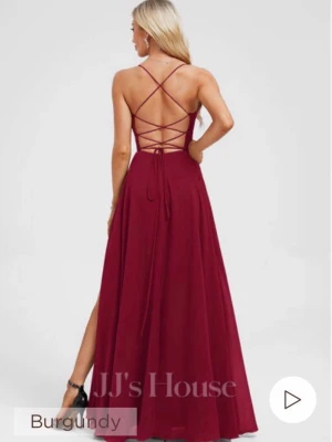 Vinröd långklänning med snörning - Elegant vinröd långklänning från JJ's House med smala axelband, v-ringning och öppen rygg med snygg snörning. Klänningen har en hög slits framtill och ett svepande fall. Perfekt för dig som vill sticka ut på bal eller fest.
