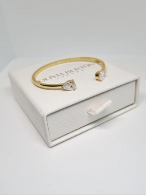 18k guldpläterat armband - Stilrent guldfärgat armband med två droppformade klara stenar i varje ände. Armbandet är stelt och har en elegant, minimalistisk design som passar perfekt till din smyckessamling. Lådan ingår ej.