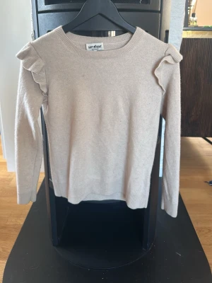 Beige cashmeretröja med volang Soft Goat - Snygg beige cashmere tröja från Soft Goat med volangdetaljer på axlarna. Tröjan har rund halsringning, långa ärmar och är gjord i ett mjukt material som känns lyxigt. Perfekt för dig som gillar en stilren look med en twist.