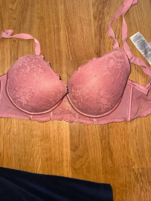 Rosa push-up bh med spetsdetaljer - Söt rosa push-up bh med vadderade kupor och fina spetsdetaljer framtill. Justerbara axelband och hakknäppning bak. Materialet är en kombination av spets och mjuk textil för extra komfort. 