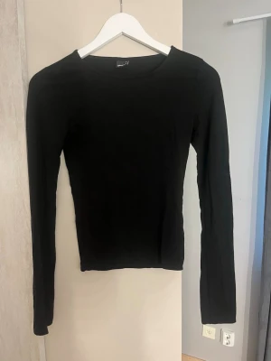 Svart långärmad topp/sweter - En enkel och stilren svart långärmad topp med rund halsringning. Perfekt att matcha med jeans eller kjol för en clean look. Tunn och mjuk i materialet, passar bra till lager-på-lager.