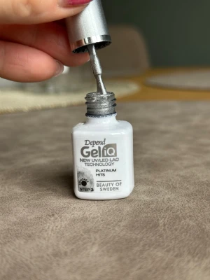 Depend GeliQ Platinum Hits nagellack - Snyggt silvrigt nagellack från Depend GeliQ-serien med UV/LED-teknologi. Färgen heter Platinum Hits och ger en metallisk, glittrande finish. Perfekt för dig som vill ha ett trendigt och hållbart resultat. Kommer i en liten fyrkantig flaska med silverfärgat lock.