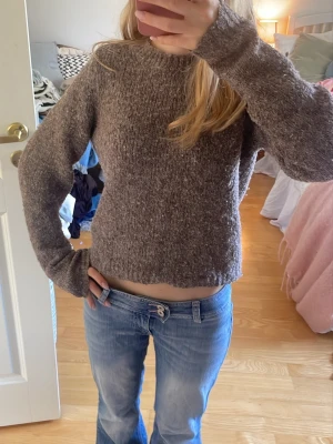Brun stickad  - Mysig brun stickad tröja med rund hals och långa ärmar. Tröjan har en något boxig passform och är tillverkad i ett mjukt, fluffigt material som känns skönt mot huden. Perfekt för kyliga dagar och enkel att matcha med jeans eller kjol.