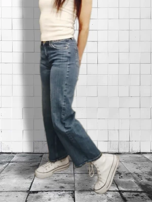 Blå raka jeans med hög midja - Snygga blå jeans med rak passform och hög midja. Jeansen har klassisk femficksdesign och subtila slitningar för en avslappnad look. Perfekta till sneakers och crop tops. Materialet är denim i bomull.