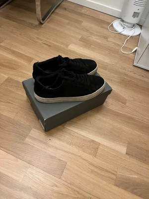 Svarta sneakers i mocka med snörning - Snygga svarta sneakers i mocka med klassisk vit sula och snörning. Perfekta för dig som gillar en stilren och enkel look. Passar till det mesta och är lätta att matcha med olika outfits.