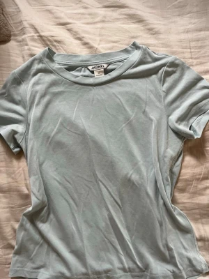 Ljusblå t-shirt från Monki - En basic ljusblå t-shirt från Monki i mjukt och stretchigt material. Modellen har rund halsringning och korta ärmar, perfekt för en avslappnad och stilren look. Enkel att matcha med jeans eller kjol.