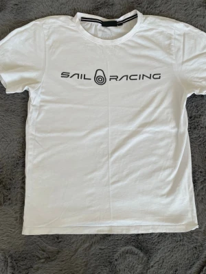 Vit Sail Racing t-shirt - !DET STÅR 160cm MEN DEN ÄR MINDRE I STORLEK! Vit t-shirt från Sail Racing med svart logotyptryck på bröstet och en liten logga i nacken. Klassisk rund hals och korta ärmar. Tillverkad i mjuk bomull för en skön känsla.