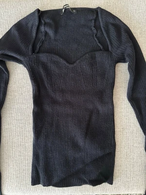 Svart stickad långärmad topp Bik Bok - Snygg svart ribbad topp från Bik Bok med lång ärm och sweetheart-urringning. Figurnära passform och stretchigt material som sitter bekvämt. Perfekt till jeans eller kjol för en trendig look.