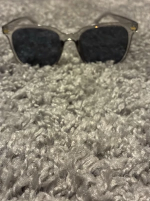 Transparenta solglasögon med svarta glas - Snygga solglasögon med transparent båge och mörka svarta glas. Klassisk fyrkantig form som passar till de flesta stilar. Perfekta för att ge din look en cool touch i solen.