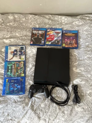 PlayStation 4 med handkontroll och spel - PlayStation 4 konsol i svart, med en svart DualShock 4 handkontroll och strömkabel. Medföljer sex PS4-spel: Call of Duty Black Ops III, Cars 3, Minecraft, FIFA 23, Crash Bandicoot och Minecraft Dungeons. Perfekt för gaming och multiplayer.