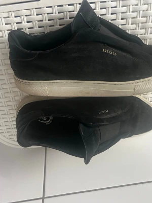 Svarta sneakers från Axel Arigato - Svarta sneakers från Axel Arigato i mocka med diskret logga i guld på sidan. Skorna har en vit, tjock sula och en stilren, minimalistisk design utan snörning. Perfekta för en clean och modern look.kom gärna med prisförslag 