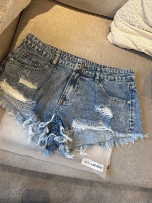 Nya i förpackning! Blå slitna jeansshorts med fransar - Trendiga blå jeansshorts, slitna detaljer och fransig kant. Klassisk femficksmodell i bomull som ger en cool och avslappnad look. Perfekta för varma sommardagar och festivaler.