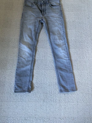Nudie lean dean w28 - Snygga ljusgrå slim fit jeans med klassisk femficksdesign och diskreta slitningar. Jeansen har raka ben och normal midja, perfekta för en avslappnad och trendig look. Materialet är mjukt och stretchigt för extra komfort. En liten defekt i grenen men är en lätt lagning av dig eller Nudies grattis lagningar.