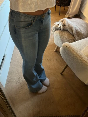 Ljusblå bootcut jeans - Säljer ett par ljusblå bootcut jeans med klassisk femficksdesign och normal midja. Jeansen har en lätt utsvängd passform nedtill och är tillverkade i mjukt denimtyg. Perfekta för en avslappnad och trendig look. Lite spruckna på baksidan av jeansen som ja har fotat 