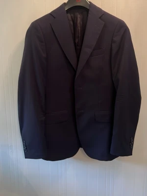 Mörkblå kavaj från Cavaliere - Stilren mörkblå kavaj från Cavaliere i slim fit-modell. Kavajen är tillverkad i 100% ull och har klassiska slag, tre fickor framtill samt knappar vid ärmsluten. Perfekt för en dressad look.
