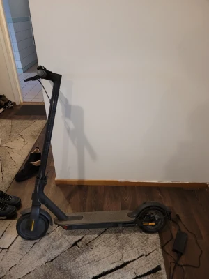 Svart elscooter med laddare - Elektrisk scooter i svart med grått ståbräde och gula detaljer på hjulen. Kommer med laddare. Stilren design och smidig att använda för kortare transporter.