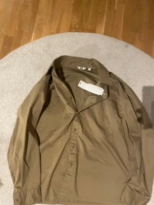 Beige skjorta från Uniqlo U L - Säljer en stilren beige skjorta från Uniqlo U i storlek L. Aldrig använd helt ny med prislapp