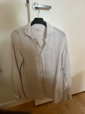 Randig skjorta från Jack & Jones - Klassisk långärmad skjorta i linne från Jack & Jones i vitt med tunna grå ränder. Skjortan har knappar framtill och en avslappnad krage. 