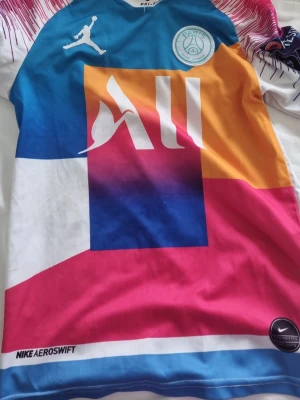 PSG x Jordan färgglad matchtröja - Fet PSG-matchtröja i samarbete med Jordan och Nike. Tröjan har en cool färgblockdesign i blått, rosa, orange och vitt med PSG-logga och Jordan-logga på bröstet. Tillverkad i lätt och ventilerande Dri-FIT-material, perfekt för fotboll eller träning.