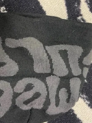 Svart mössa med grå text - Snygg svart mössa med grått mönster och text i stickat material. Perfekt accessoar för att hålla värmen och ge en cool touch till din outfit. Mjuk och stretchig passform som sitter skönt på huvudet.