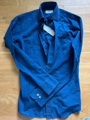 Blå skjorta från John Henric - Snygg blå skjorta från John Henric i klassisk modell med lång ärm och knappar framtill. Skjortan är tillverkad i bomull och har en stilren krage. Perfekt för dig som gillar en enkel men stilfull look.