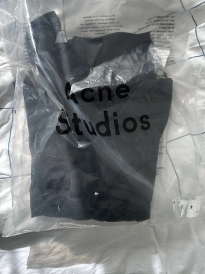 Svart t-shirt från Acne Studios - En svart t-shirt från Acne Studios med klassisk passform och rund hals. T-shirten har en stilren design med Acne Studios-loggan tryckt framtill. Perfekt basplagg för en trendig och enkel look.