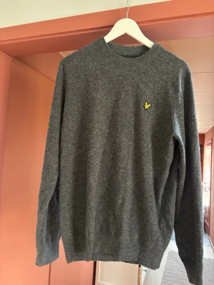 Grå tröja från Lyle & Scott - Mörkgrå stickad tröja från lyle & scott i storlek L. Riktig skön till en kall sommarkväll