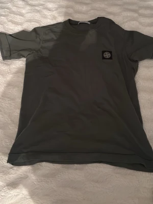 Grå t-shirt från Stone Island - Snygg grå t-shirt från Stone Island med klassisk rund hals och ikonisk patch på bröstet. Tillverkad i mjuk bomull och har en clean, enkel design som passar till allt. Perfekt för dig som gillar streetwear och vill ha något stilrent.