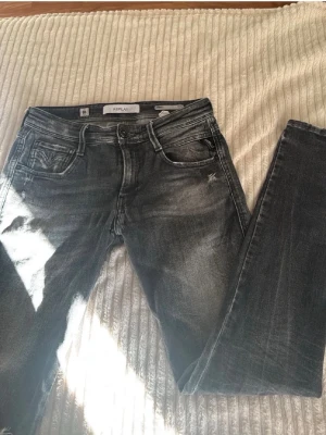 Gråa Replay Jeans Med Slitningar  - Säljer ett par grå jeans från Replay med slitningar och tvättade detaljer. Modellen är slim fit med klassisk femficksdesign och dragkedjegylf. Snyggt slitna partier på låret och knät ger en cool look. Perfekta för dig som gillar streetstyle.