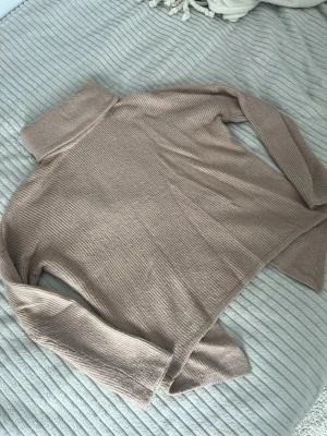 Beige polotröja i ribbstickat - Mysig beige polotröja i ribbstickat material med lång ärm och hög krage. Tröjan har en avslappnad passform och är perfekt för lager på lager. Materialet känns mjukt och följsamt, vilket gör den skön att bära under kyliga dagar.