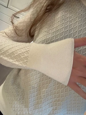 Vit stickad tröja - Snygg vit stickad tröja med diskret rutmönster och breda ribbade muddar vid ärmslut och nederkant. Tröjan har rund halsringning och är långärmad. Helt oanvänd🙏🏻🙏🏻🙏🏻