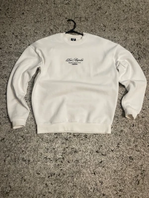 Vit sweatshirt från FSBN  - Vit sweatshirt från FSBN med broderat tryck på bröstet där det står 'Los Angeles Beverly Hills - Calif.' i svart. Tröjan har rund halsringning och långa ärmar. Perfekt för en clean och avslappnad stil.