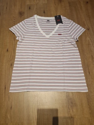 Randig v-ringad t-shirt från Levi's - Säljer en randig t-shirt från Levi's med v-ringning och korta ärmar. T-shirten har en liten Levi's-logga på bröstet och är tillverkad i mjuk bomull. Perfekt för en avslappnad och stilren look.