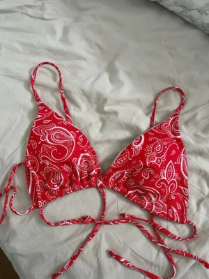 Röd bikini överdel storlek M - Röd mönstrad bikini överdel i strl L (passar mer som en M) Använd 1 gång. Mycket bra skick förutom att den fått nån knappt synlig missfärgning (se sista bilden)