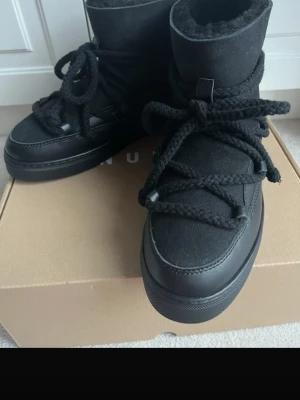 Svarta Inuikii boots  - Säljer ett par svarta Inuikii boots med grova snören och rund tå. Skorna är tillverkade i en mix av mocka och skinn, med mjuk päls på insidan för extra värme. Klassisk siluett med platt sula och snygga detaljer runt hela skon. Perfekta för kalla dagar. Använda men jätte bra skick