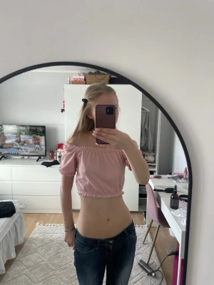 Ljusrosa offshoulder croppad topp - Säljer en ljusrosa croppad topp med offshoulder-design och korta puffärmar. Toppen har elastiska band vid axlar och nederkant för en snygg passform. Perfekt för dig som vill ha en söt och trendig look.