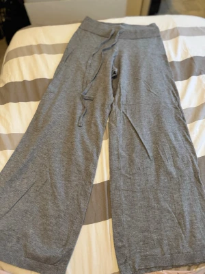 Grå soft touch från Gina Tricot - Säljer ett par grå mjukisbyxor från Gina Tricot med bred resår i midjan och dragsko. Byxorna har raka, vida ben och är gjorda i mjukt och bekvämt material. Perfekta för chill dagar hemma eller när du vill ha en avslappnad stil.