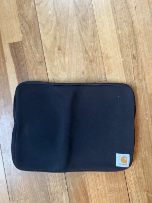 Svart laptopfodral från Carhartt - Snyggt svart laptopfodral från Carhartt med dragkedja runt om och diskret logga i hörnet. Fodralet är tillverkat i Carhartts classics Car-lux material. Passar datorer upp till 15”.  Små fläckar på baksidan, syns mindre i verkligheten. 