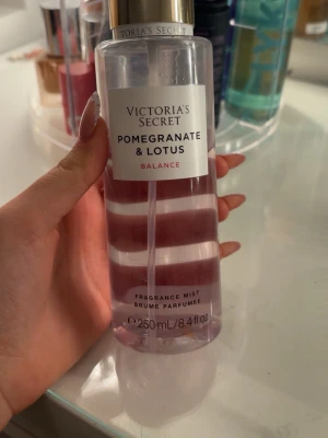 Victoria's Secret Pomegranate & Lotus mist - Fr armist från Victoria's notable Secret i doften Pomegranate & Lotus. Flaskan är genomskinlig med rosa vätska och har ett elegant guldigt lock. Rymmer 250 ml och har en stilren etikett framtill. Perfekt för dig som gillar fräscha och fruktiga dofter.