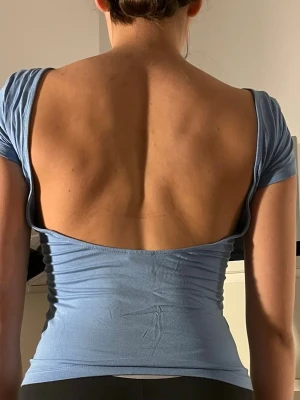 Ljusblå topp med öppen rygg - Snygg ljusblå topp med tight passform och korta ärmar. Toppen har en riktigt öppen rygg som ger en cool look. Perfekt att styla med jeans eller kjol. Mjuk och stretchig i materialet för skön känsla hela dagen.