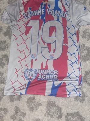 Barcelona Lamine Yamal matchtröja - Snygg Barcelona fotbollströja med Lamine Yamal och nummer 19 på ryggen. Tröjan är vit med röda och blå detaljer, klubbmärke och Nike-logga framtill samt sponsortryck från Spotify. Tillverkad i lätt och ventilerande Dri-FIT-material.