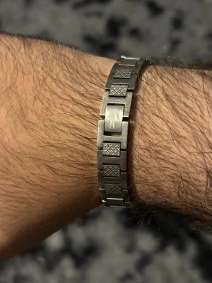 Silverfärgat armband från Lacoste - Snyggt armband i silverfärgad metall från Lacoste. Länkarna har ett rutmönster och en av länkarna är graverad med Lacostes krokodilen. OBS! Den på bilden är min egen, men utseende mässigt exakt samma som den i påsen. Påsen är oöppnad o sprillans ny. Jag fick den i present, men hade redan en så jag väljer att sälja denna.
