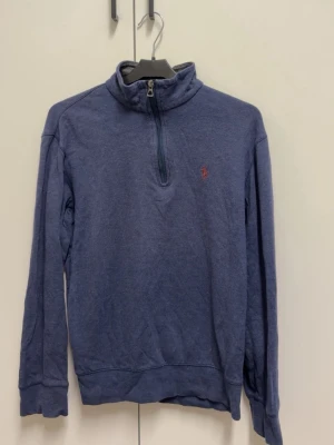 Blå halvzip tröja från Polo Ralph Lauren - Mörkblå långärmad tröja med halv dragkedja och hög krage från Polo Ralph Lauren. Liten röd logga broderad på bröstet. Perfekt för en avslappnad och stilren look.