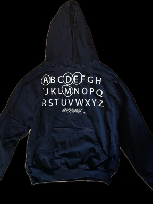 Deema hoodie  - Cool svart hoodie med stor vit alfabet-tryck på framsidan och Deema -logga Hoodien har huva och en stor magficka framtill. Perfekt för dig som gillar streetwear och vill sticka ut med en unik design. Lite mg stil på det.
